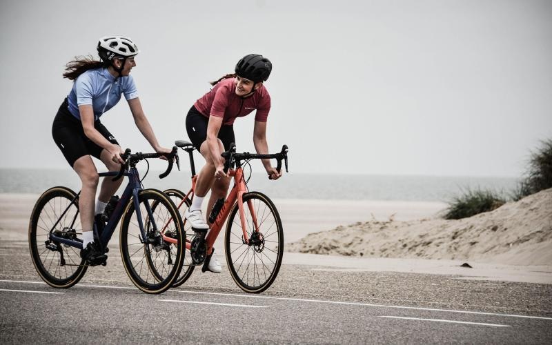 women bicycling on the road along a beach