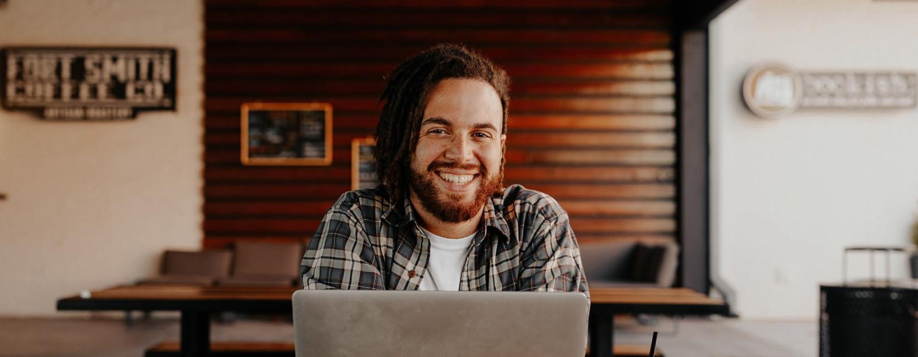 man sits with a drink in front of an open laptop in local restaurant